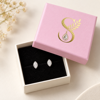 Pair of silver studs displayed inside an open pale pink gift box with black velvet lining.