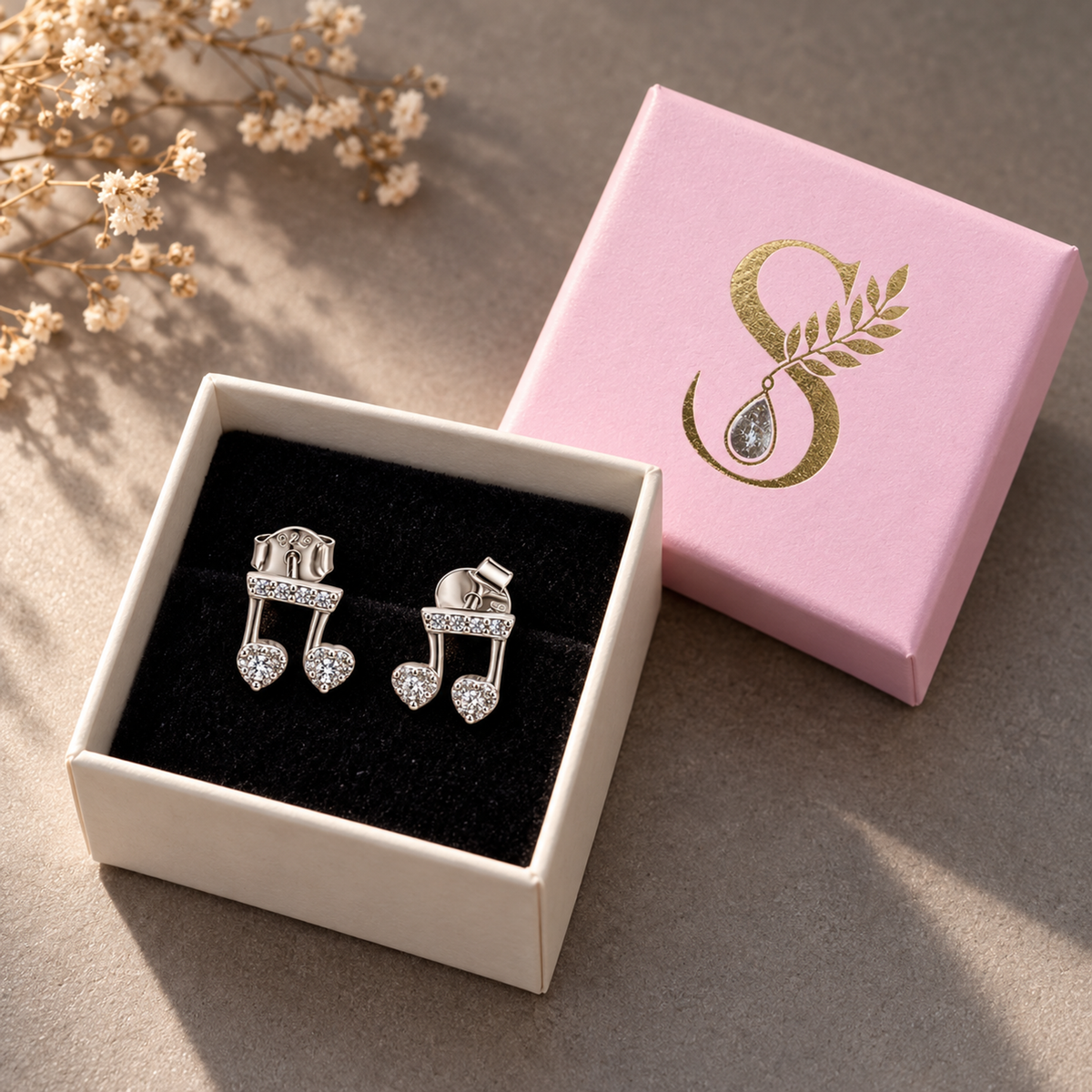 Silver musical note earrings presented inside a pale pink Silvanya jewellery box on black velvet.