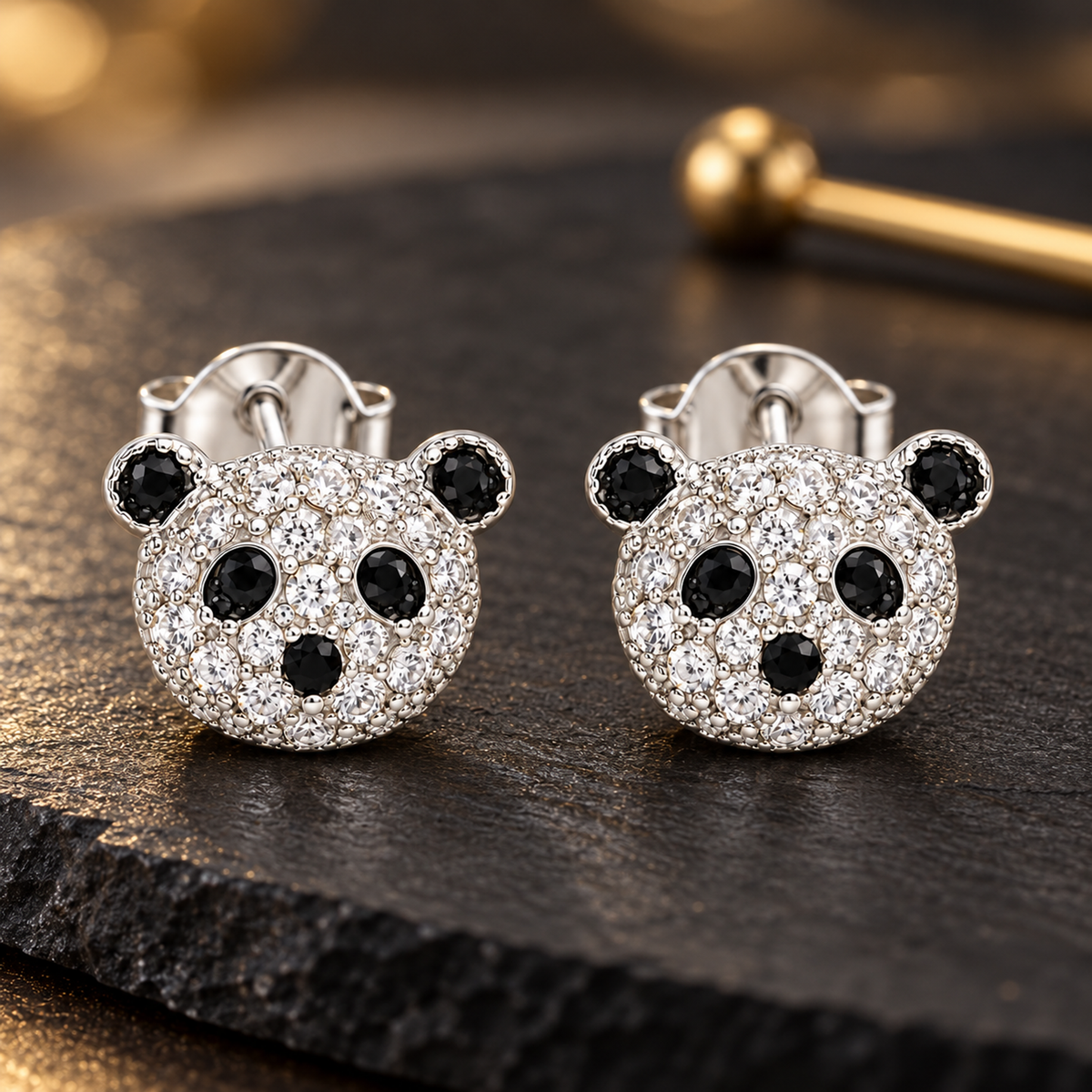 Panda face silver stud earrings resting on a matte black slate surface with soft lighting.