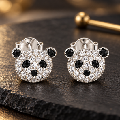 Panda face silver stud earrings resting on a matte black slate surface with soft lighting.