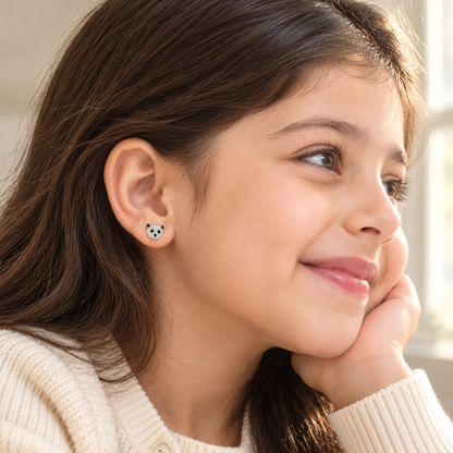 Close-up of a child wearing a silver panda stud earring in natural window light.