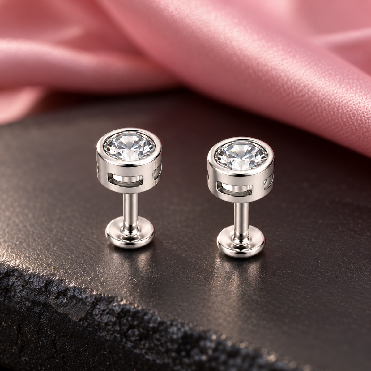 Silver stud earrings resting on textured ivory linen beside dried flowers.