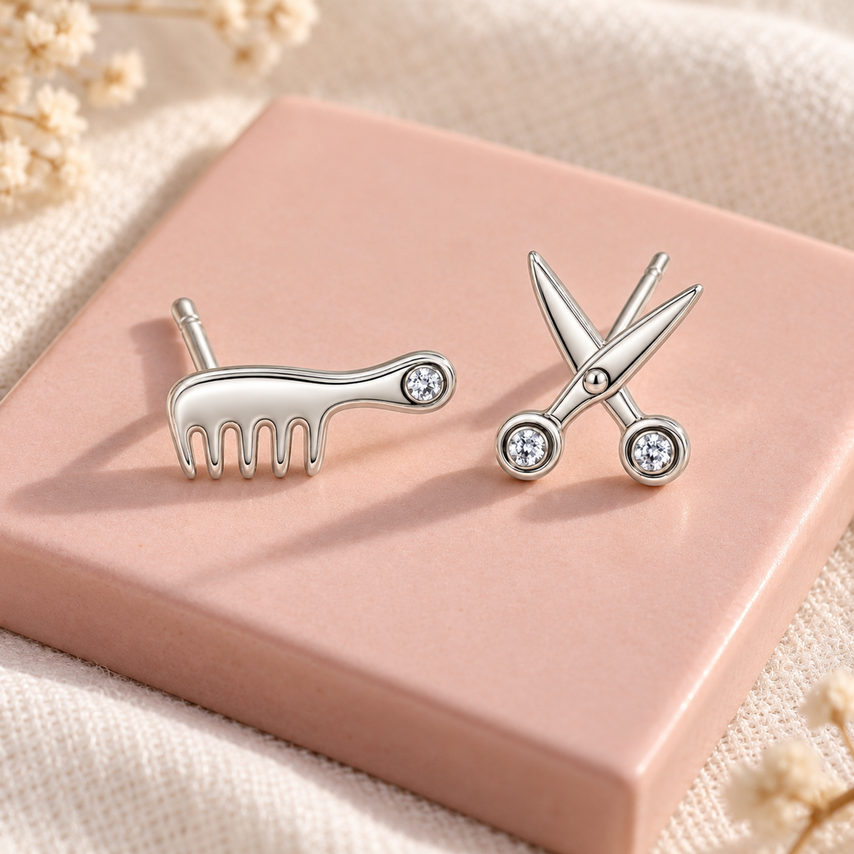 Silver comb and scissor studs resting on a blush pink ceramic tile.