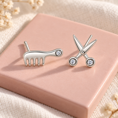Silver comb and scissor studs resting on a blush pink ceramic tile.