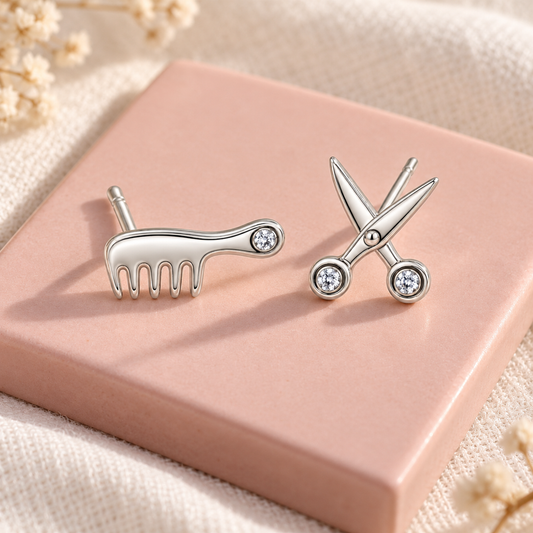 Silver comb and scissor studs resting on a blush pink ceramic tile.