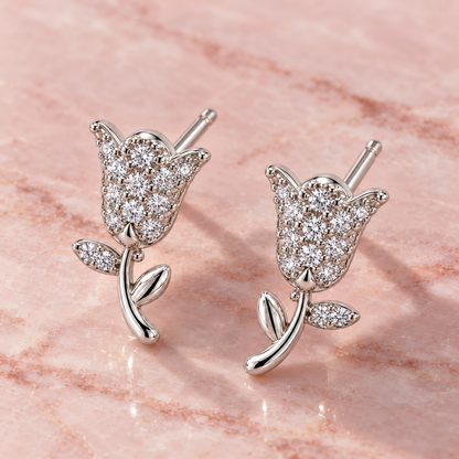 Tulip stud earrings resting on a smooth blush pink marble surface.