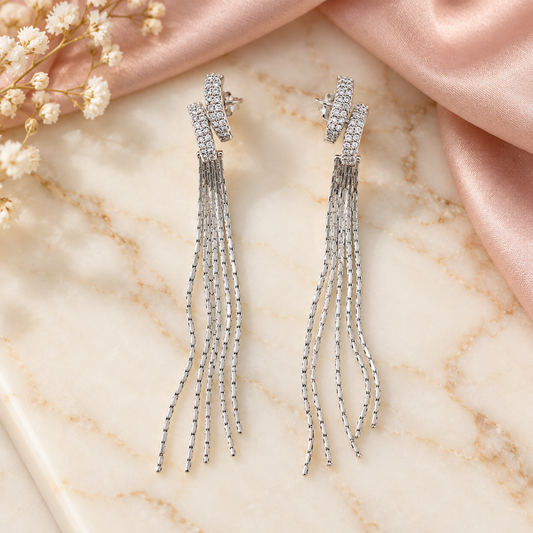 Silver tassel drop earrings laid flat on a polished ivory marble plate against blush pink fabric.