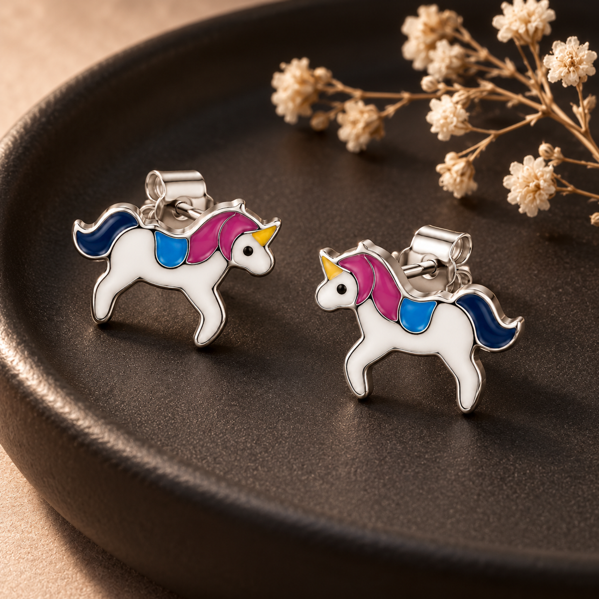 Pair of enamelled silver unicorn stud earrings resting on a circular matte black tray.