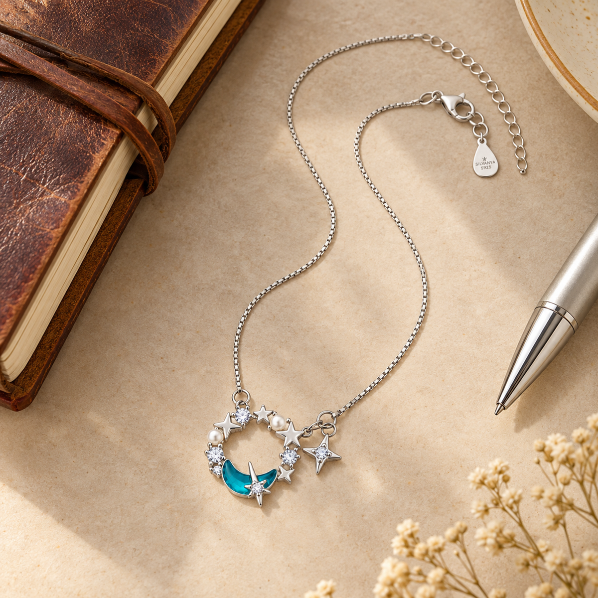 Silver celestial necklace displayed next to a notebook to showcase size.