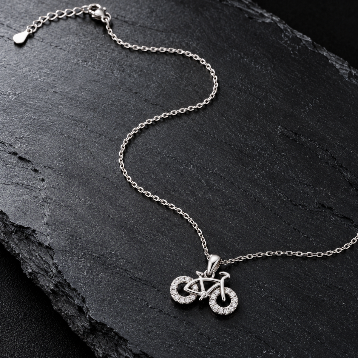 Bicycle pendant necklace laid in an S-curve on a dark matte black surface.