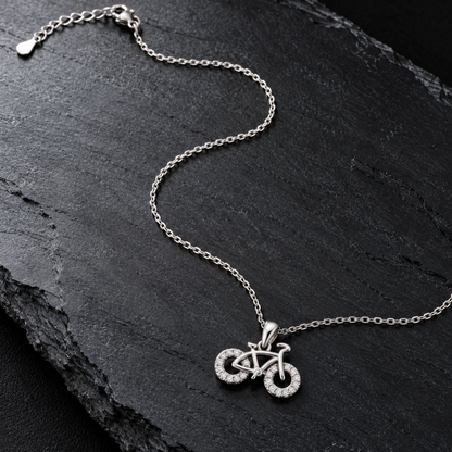 Bicycle pendant necklace laid in an S-curve on a dark matte black surface.