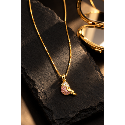 Sparkling gold bird pendant necklace presented on dark matte slate tile beside a gold compact.
