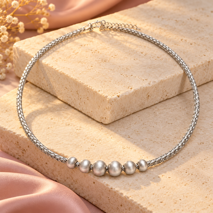 Silver braided choker resting on stacked ivory stone blocks with warm side lighting.