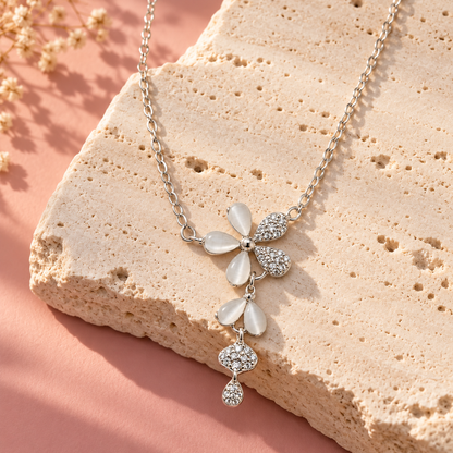 A silver flower necklace on a textured ivory stone against a soft blush pink backdrop in warm morning light.