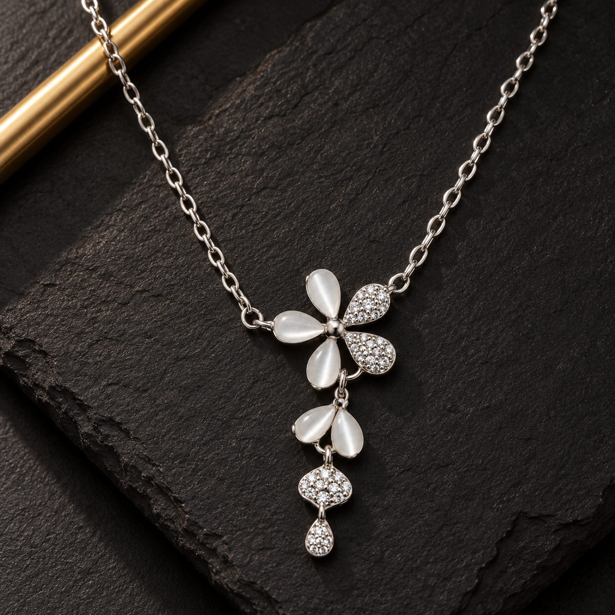A silver floral pendant necklace resting on a dark slate tile, highlighted by focused gallery lighting.
