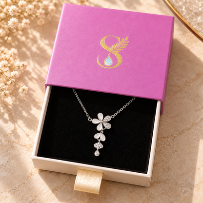 A silver flower necklace nestled inside a magenta-pink drawer-style box with a gold-foil monogram.