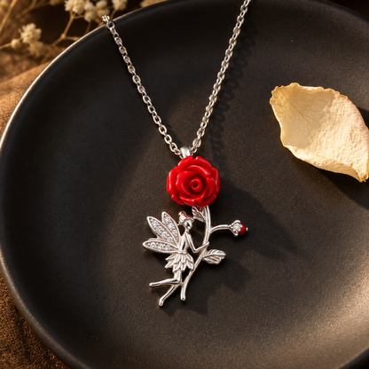 Silver fairy and rose necklace draped on a matte black plate with a single ivory petal under soft side light.