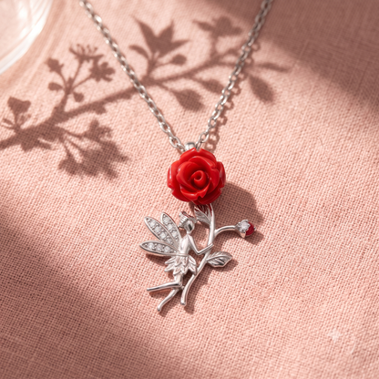 Silver fairy pendant with a red rose resting on textured blush pink fabric with dappled branch shadows.