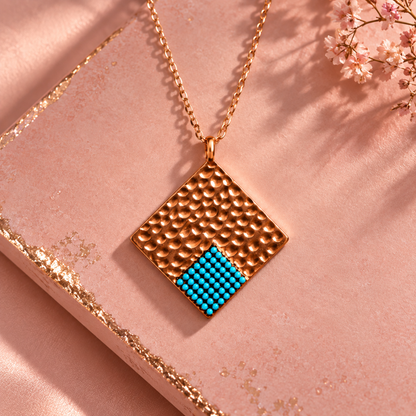 Rose gold necklace with blue beads resting on textured pink surface.