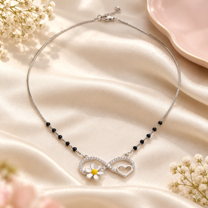 Silver infinity mangalsutra necklace resting gracefully on draped ivory silk next to a pink tray.