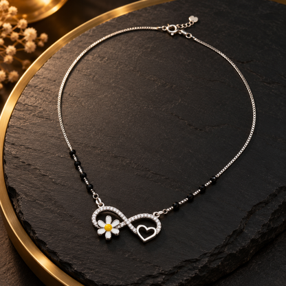 Silver infinity necklace displayed on a dark slate surface with warm lighting accents.