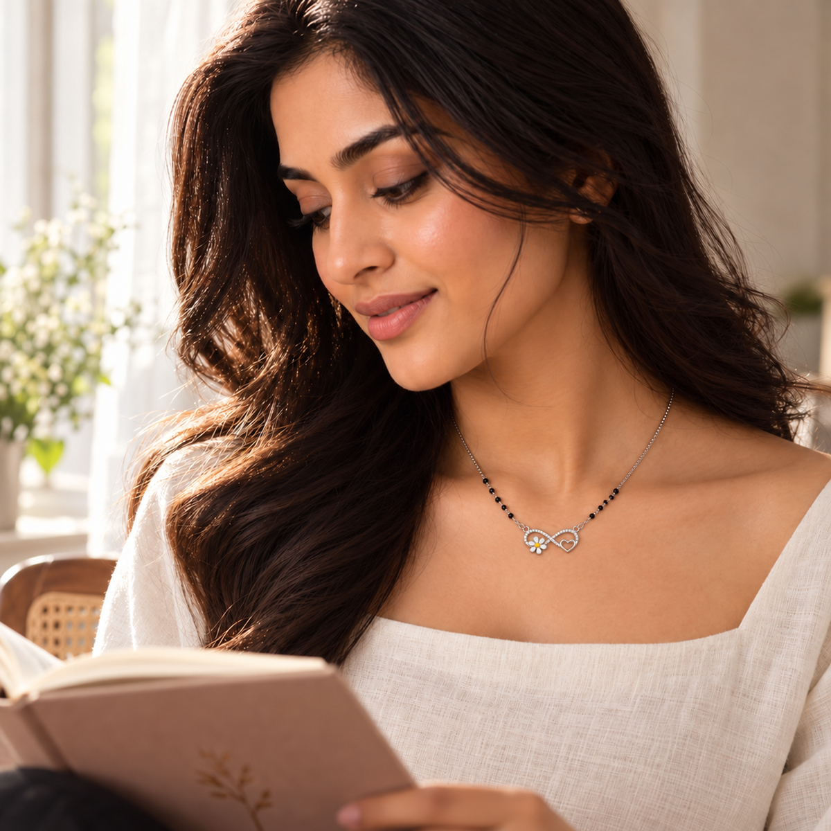 Woman in an ivory linen top wearing a silver infinity mangalsutra necklace while sitting by a sunlit window.