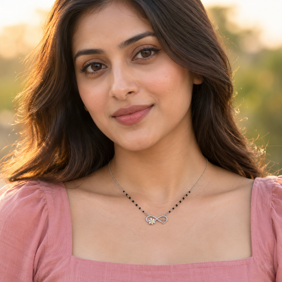 Close-up of a woman outdoors in golden hour light wearing a silver infinity pendant necklace.