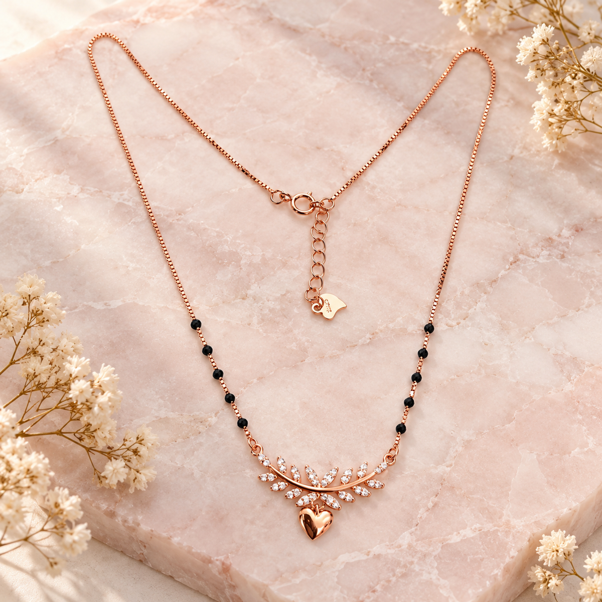 Rose gold infinity mangalsutra styled on blush pink marble with cream dried botanicals.