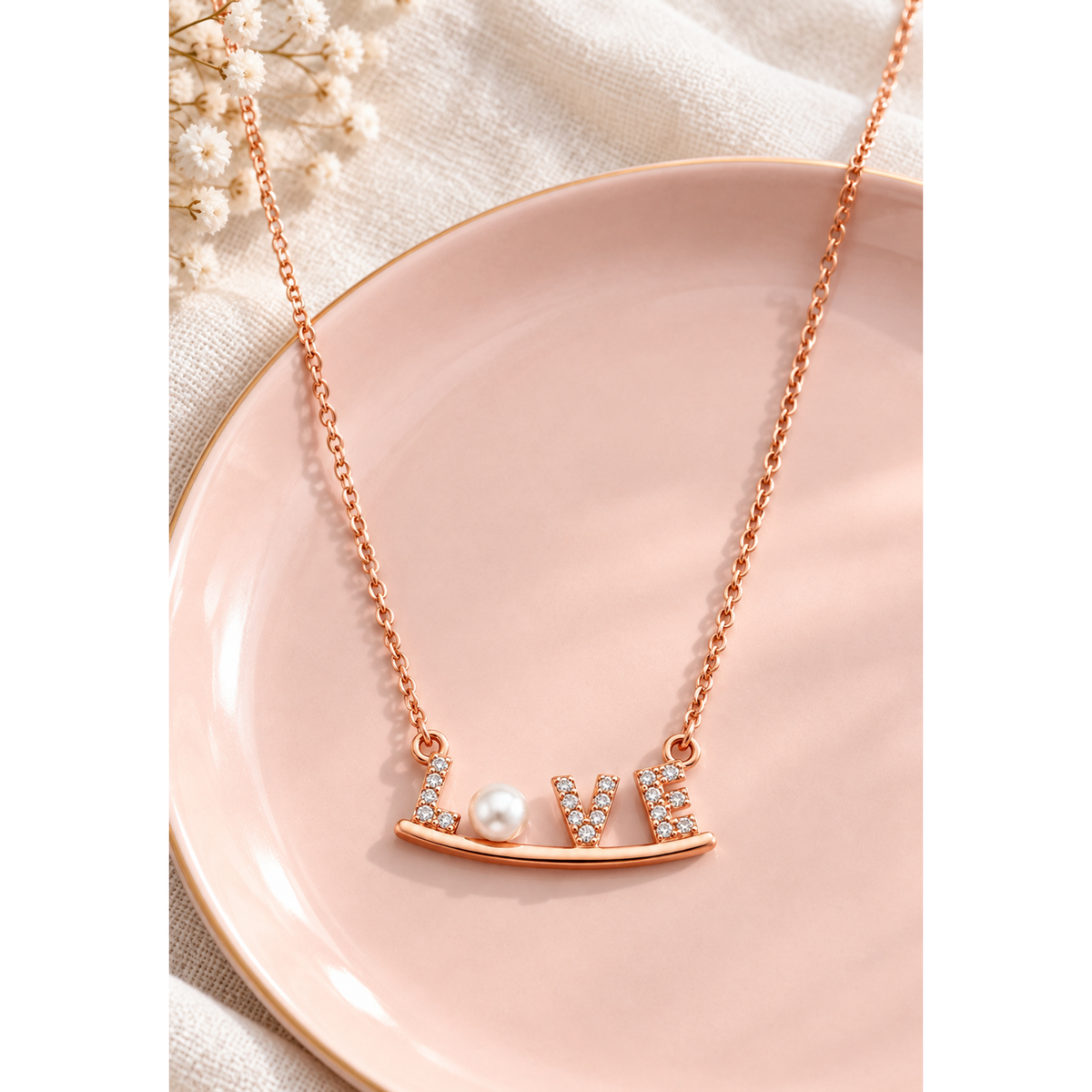 Rose gold LOVE necklace resting on a blush pink ceramic tray with ivory linen.