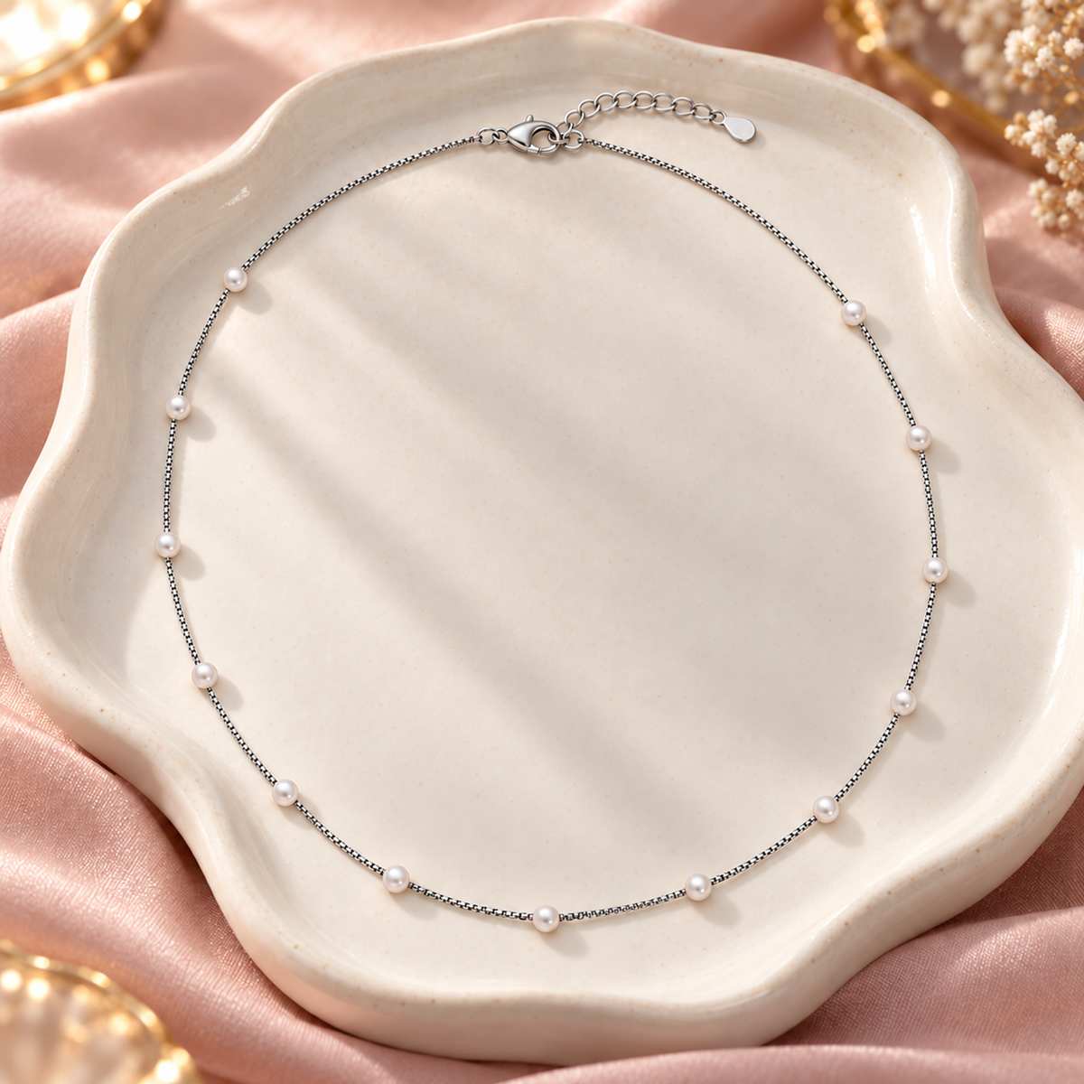 Silver pearl station necklace resting on a matte black slate surface with a dried flower.