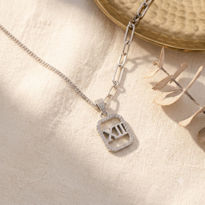 Sterling silver Roman numeral pendant resting on ivory linen next to gold decor.