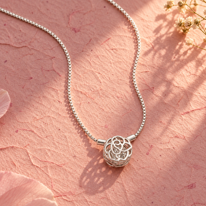 Silver rose cage necklace on textured blush pink paper under warm, angled golden hour light.