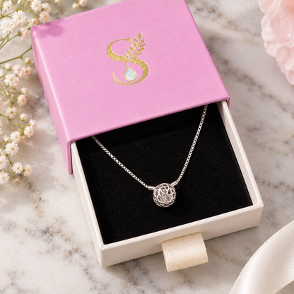 Silver rose cage pendant necklace resting inside an open pale pink Silvanya gift box with black velvet lining.