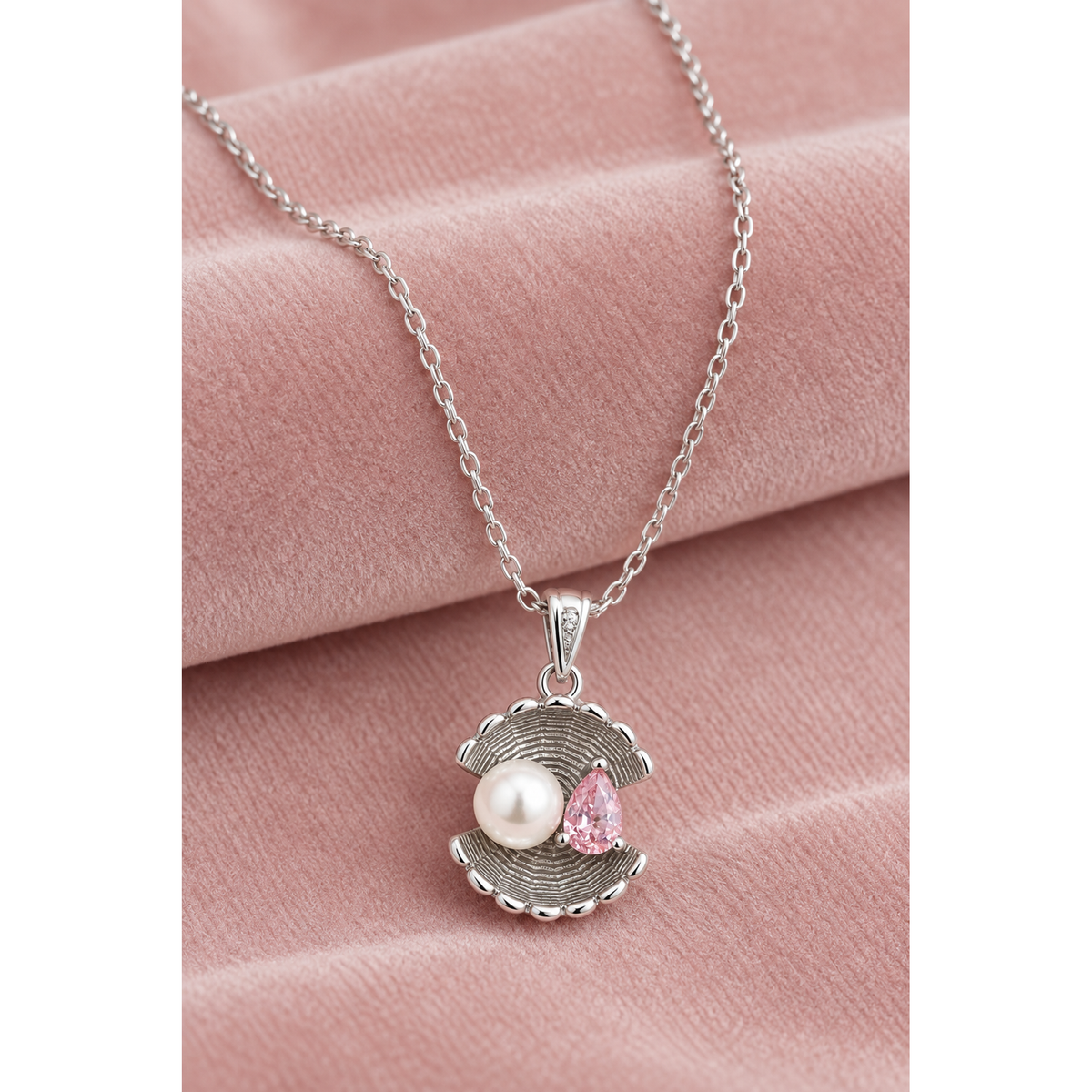 Shell pendant necklace with pearl and pink stone on a soft blush pink velvet surface.