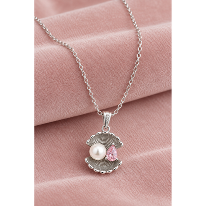 Shell pendant necklace with pearl and pink stone on a soft blush pink velvet surface.