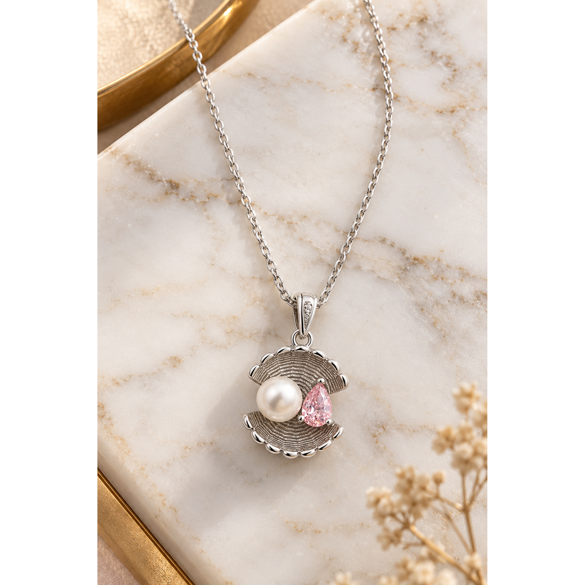 Sterling silver shell pendant necklace with pearl and pink cubic zirconia on white marble with a gold accent.