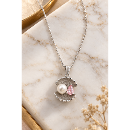 Sterling silver shell pendant necklace with pearl and pink cubic zirconia on white marble with a gold accent.