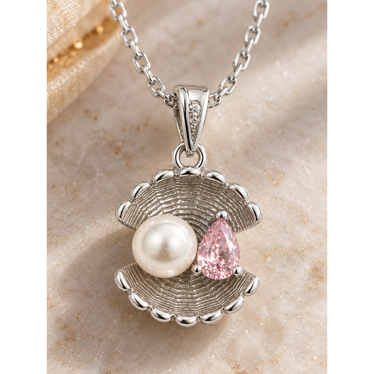 Macro view of the shell pendant, showing the ribbed silver, white pearl, and pink cubic zirconia.