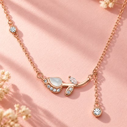 Rose gold tulip pendant chain laid on a blush pink paper surface in soft light.