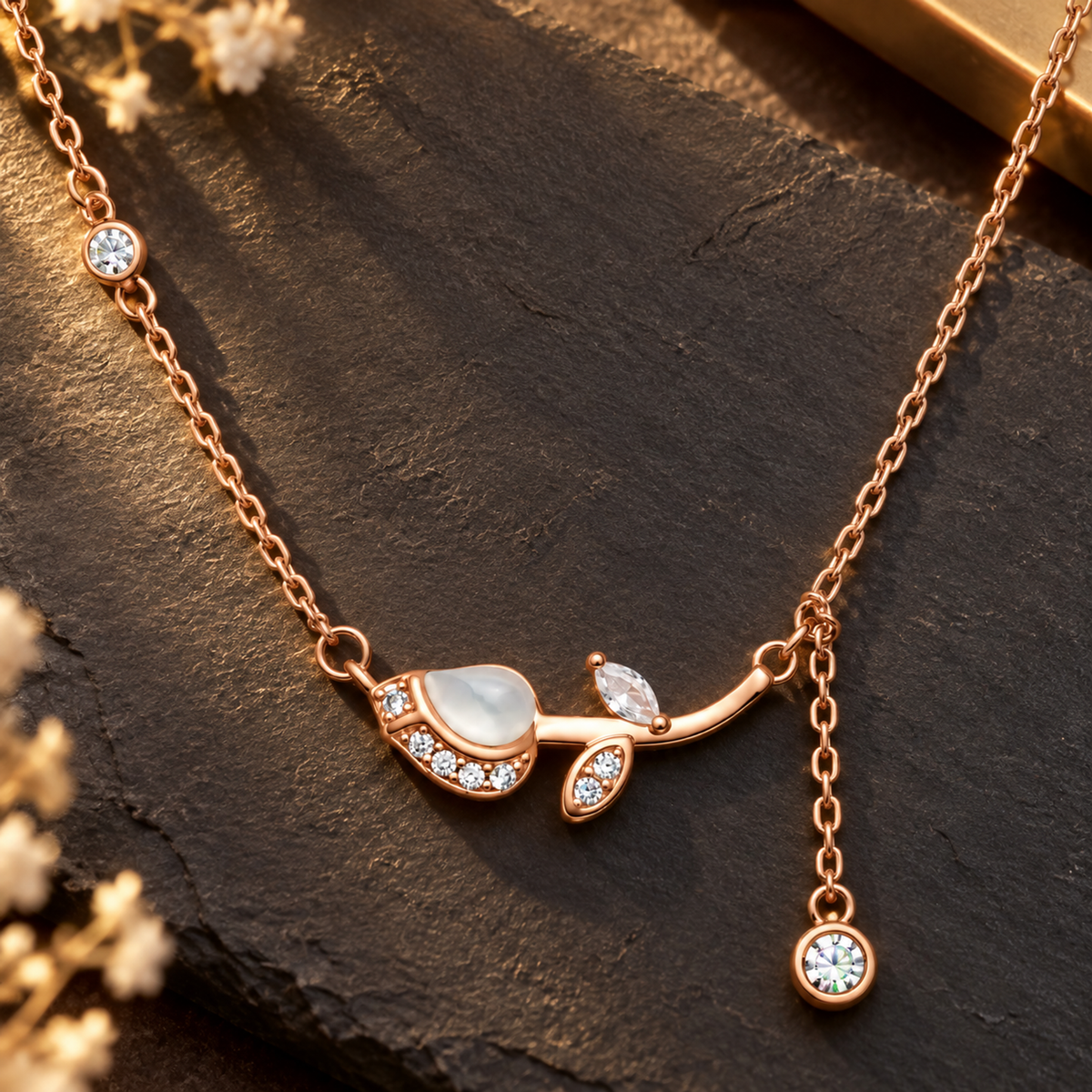 Rose gold tulip necklace resting on dark matte slate tile under warm lighting.