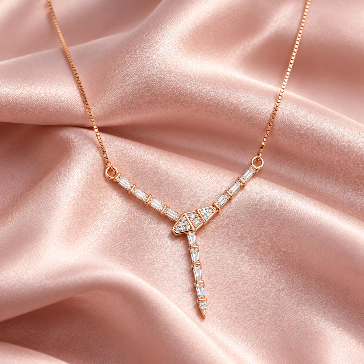 Rose gold chevron Y-necklace resting elegantly on ruffled blush pink satin fabric.