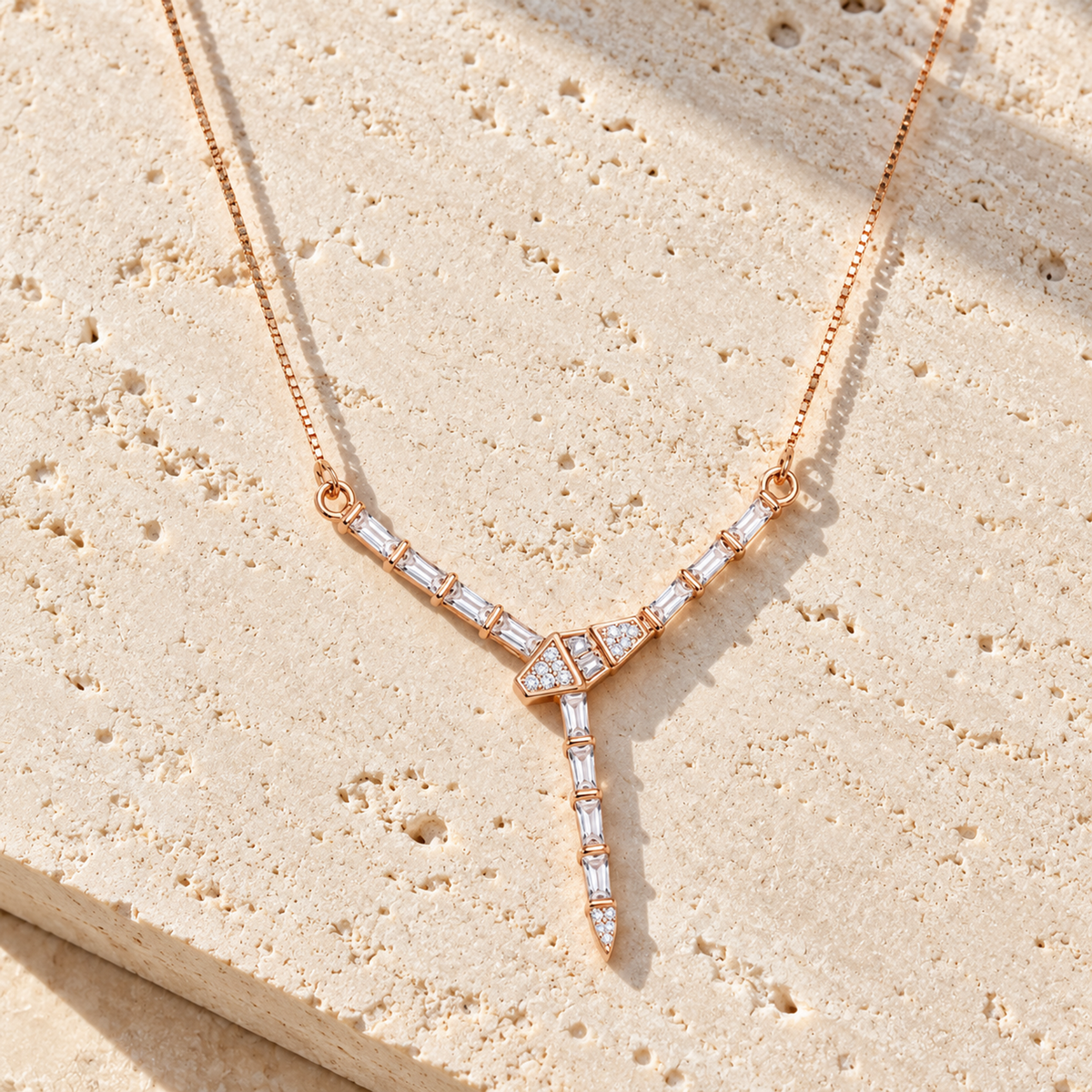 Rose gold Y-drop necklace lying on textured ivory travertine tile under warm directional sunlight.