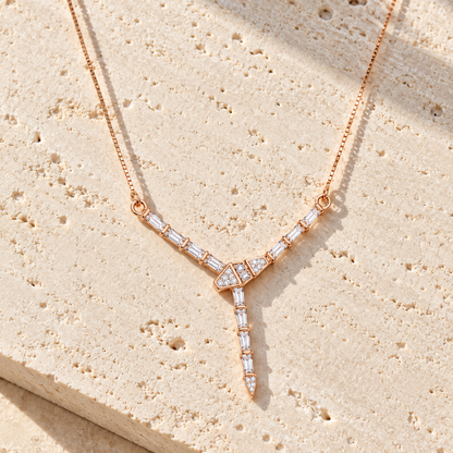 Rose gold Y-drop necklace lying on textured ivory travertine tile under warm directional sunlight.