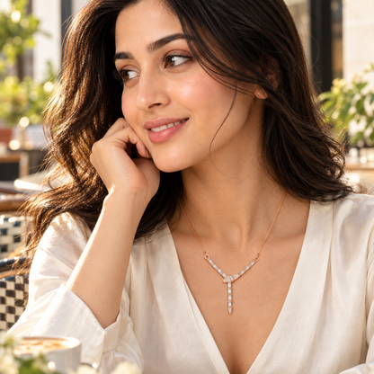Woman wearing a rose gold Y-necklace with an ivory V-neck blouse in warm natural outdoor lighting.