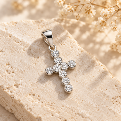 Silver bezel-set cross pendant resting gracefully on an ivory stone slab in soft sunlight.