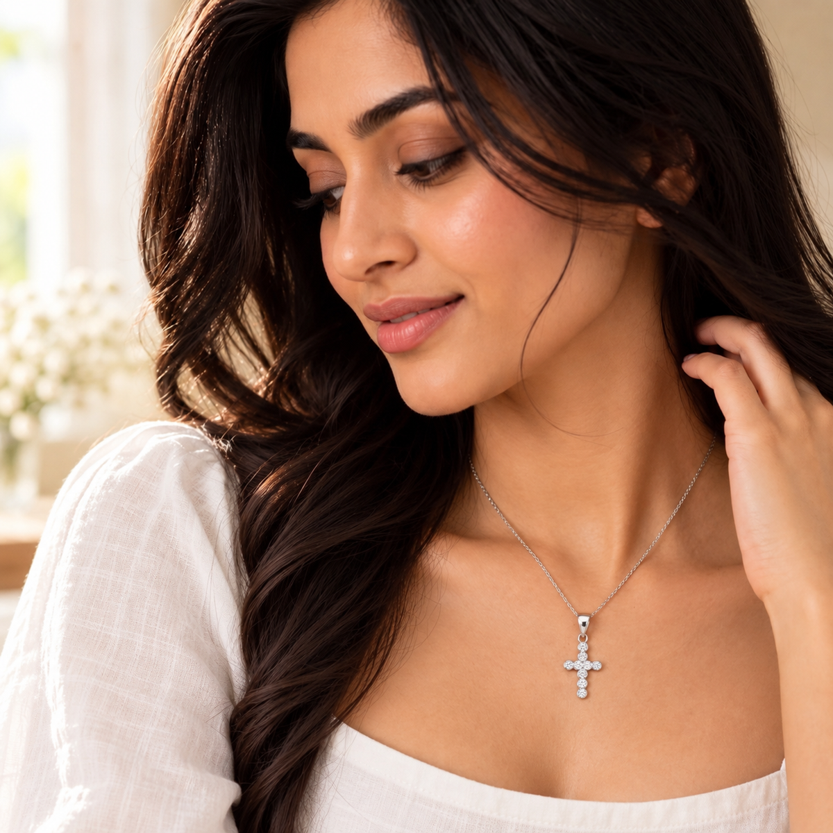 Woman wearing a silver bezel-set cross pendant against a chalk-white linen neckline.