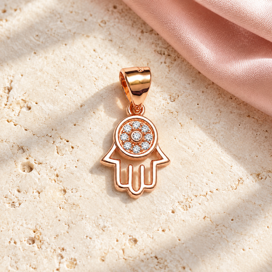 Rose gold Hamsa pendant resting on ivory stone alongside draped blush pink silk.