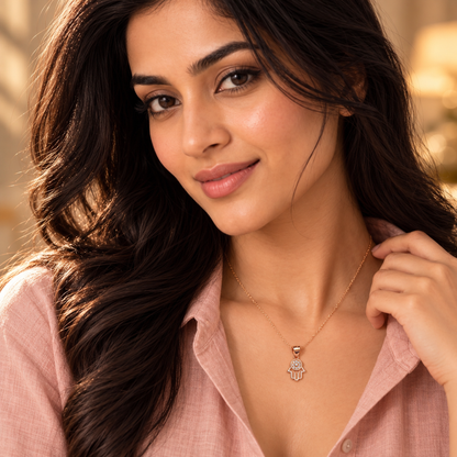 Close-up of woman wearing rose gold Hamsa pendant adjusting her blush shirt collar.