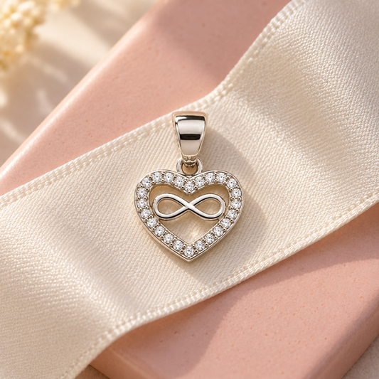 Silver infinity heart pendant resting on ivory silk and a blush pink tile.