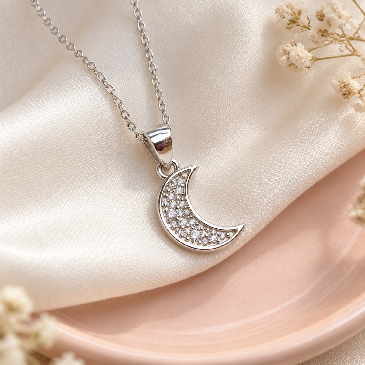 Pave crescent moon silver pendant resting on ivory silk and a blush ceramic plate.